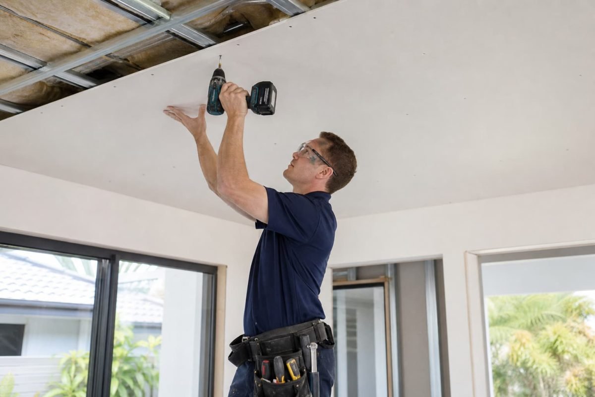 Ceiling installer securing plasterboard to ceiling framing